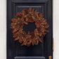Handmade holiday wreath crafted from natural brown pinecones, mounted on a dark navy blue paneled door.