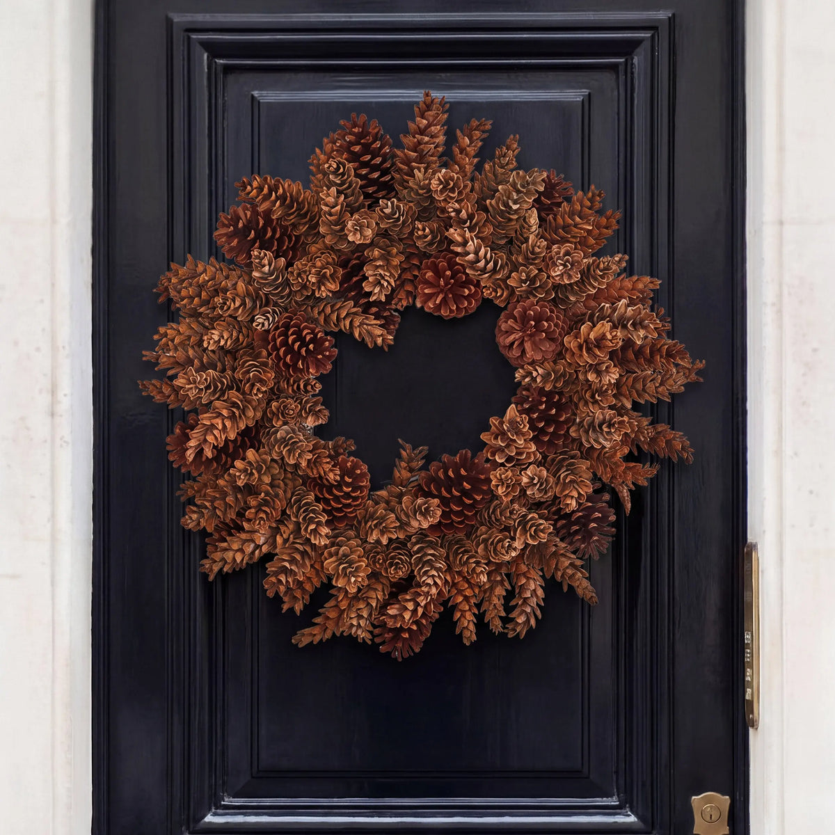 Handmade holiday wreath crafted from natural brown pinecones, mounted on a dark navy blue paneled door.