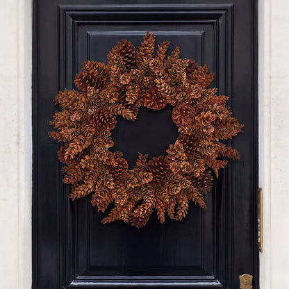 Handmade holiday wreath crafted from natural brown pinecones, mounted on a dark navy blue paneled door.