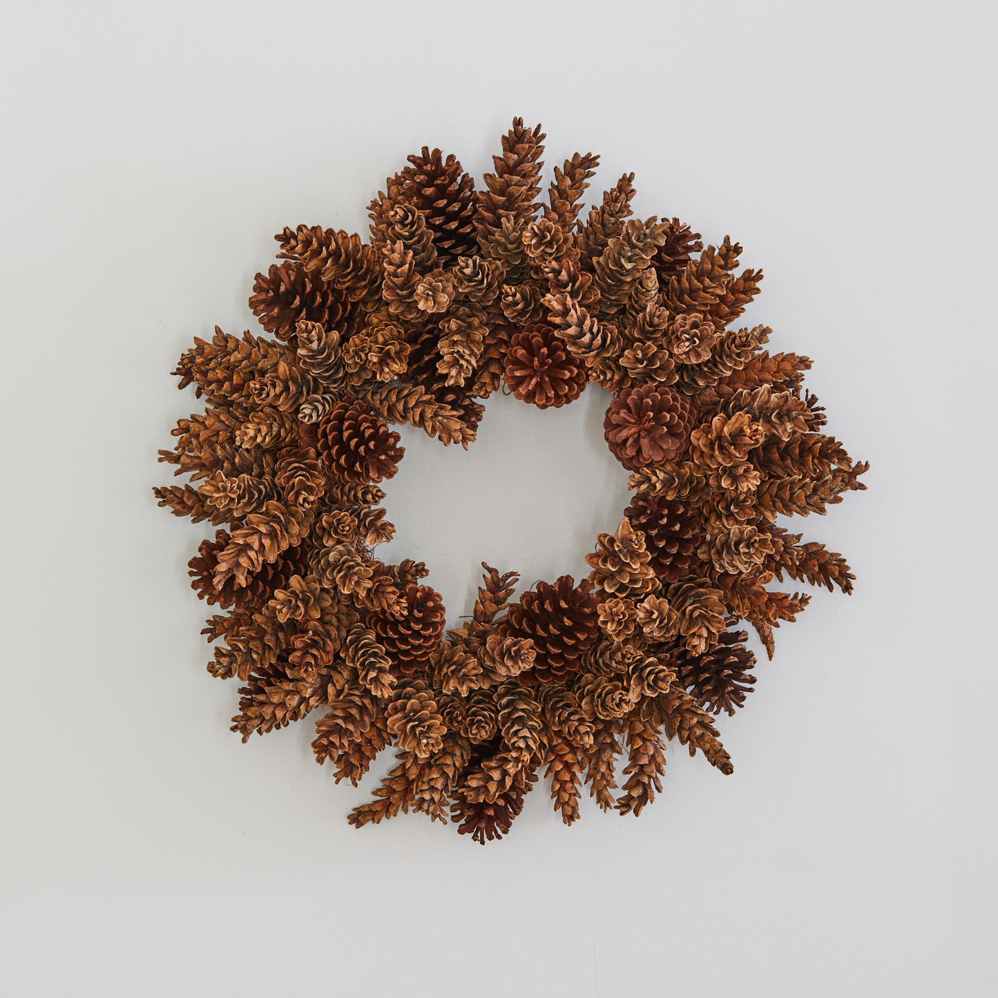 Handmade holiday wreath crafted from natural brown pinecones on a plain white background.