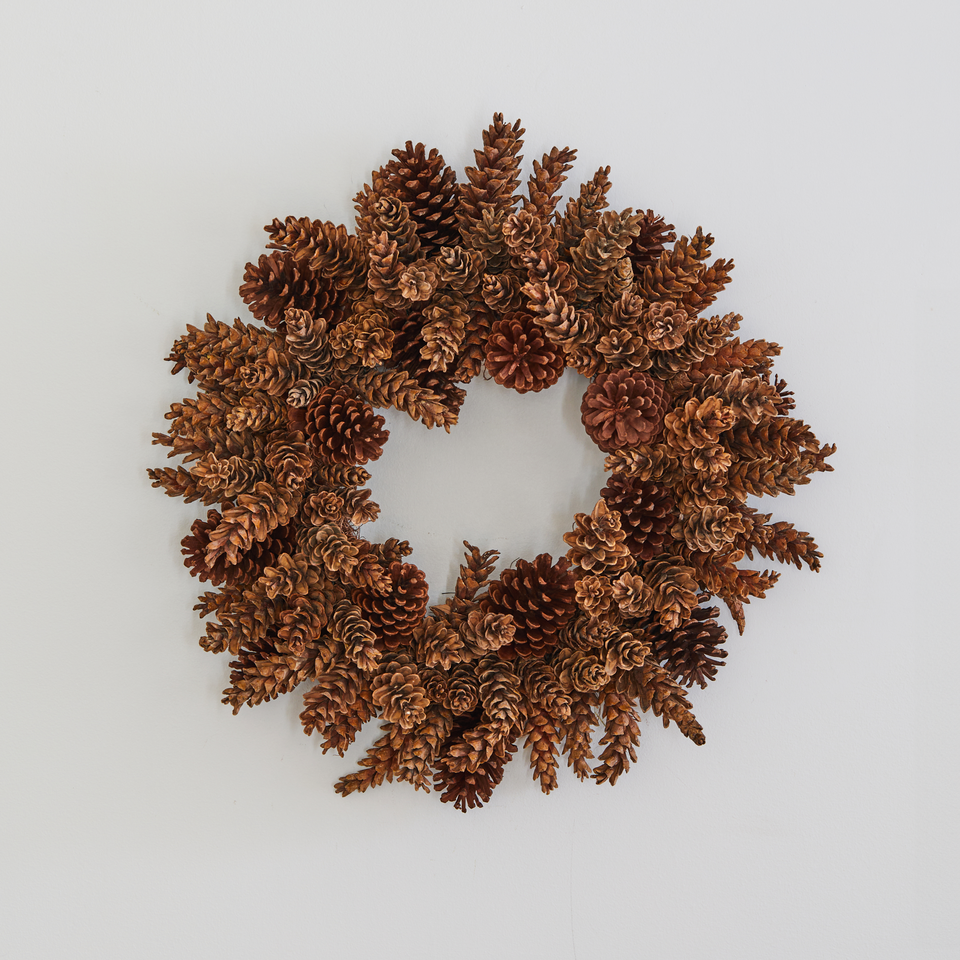 Handmade holiday wreath crafted from natural brown pinecones on a plain white background.