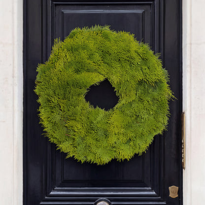 Fresh 24-inch cedar wreath with feathery green foliage hanging on a dark black front door.