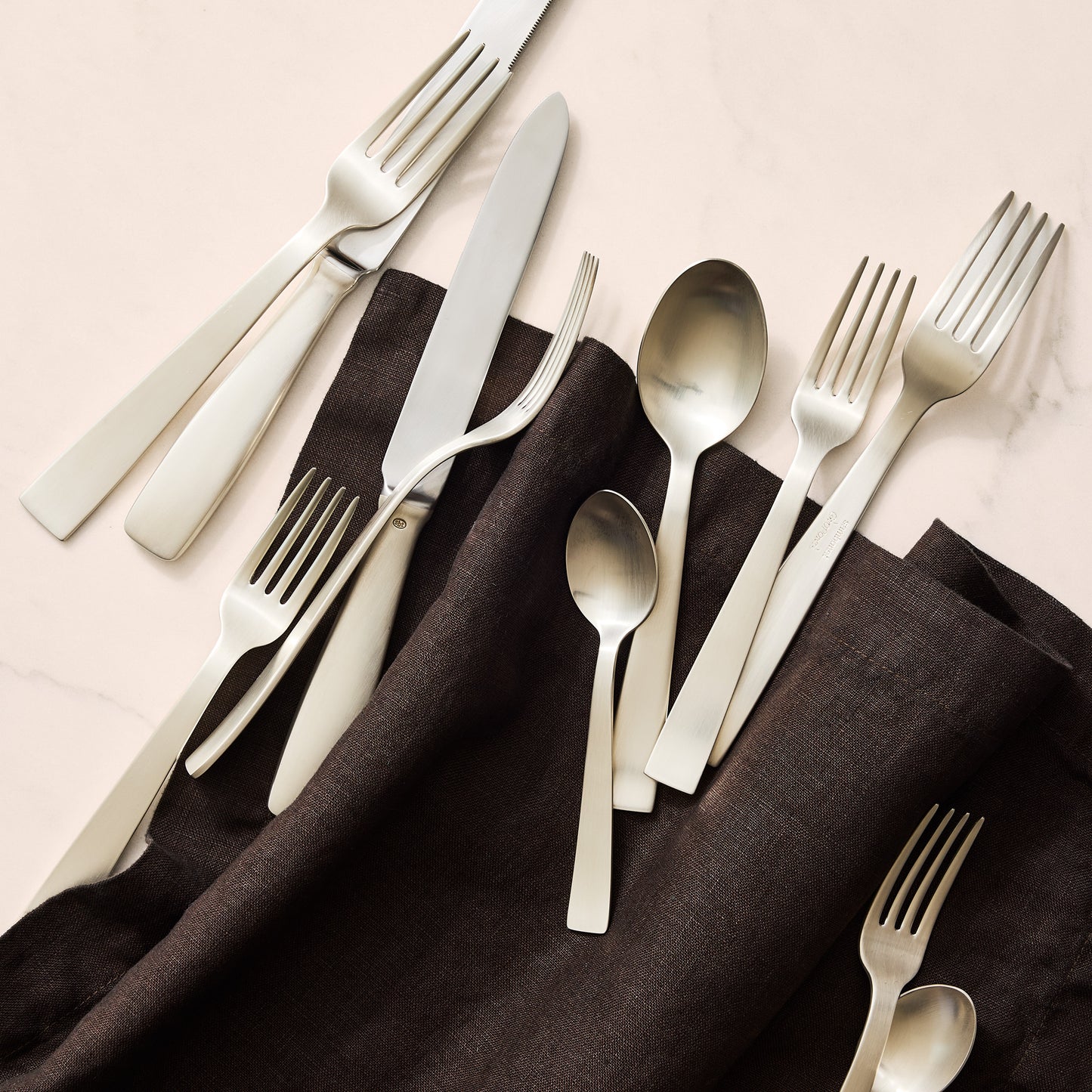 Gio Ponti 5-piece satin silverplate flatware set with monobloc knives on a dark linen napkin.