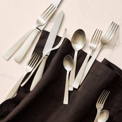 Gio Ponti 5-piece satin silverplate flatware set with monobloc knives on a dark linen napkin.