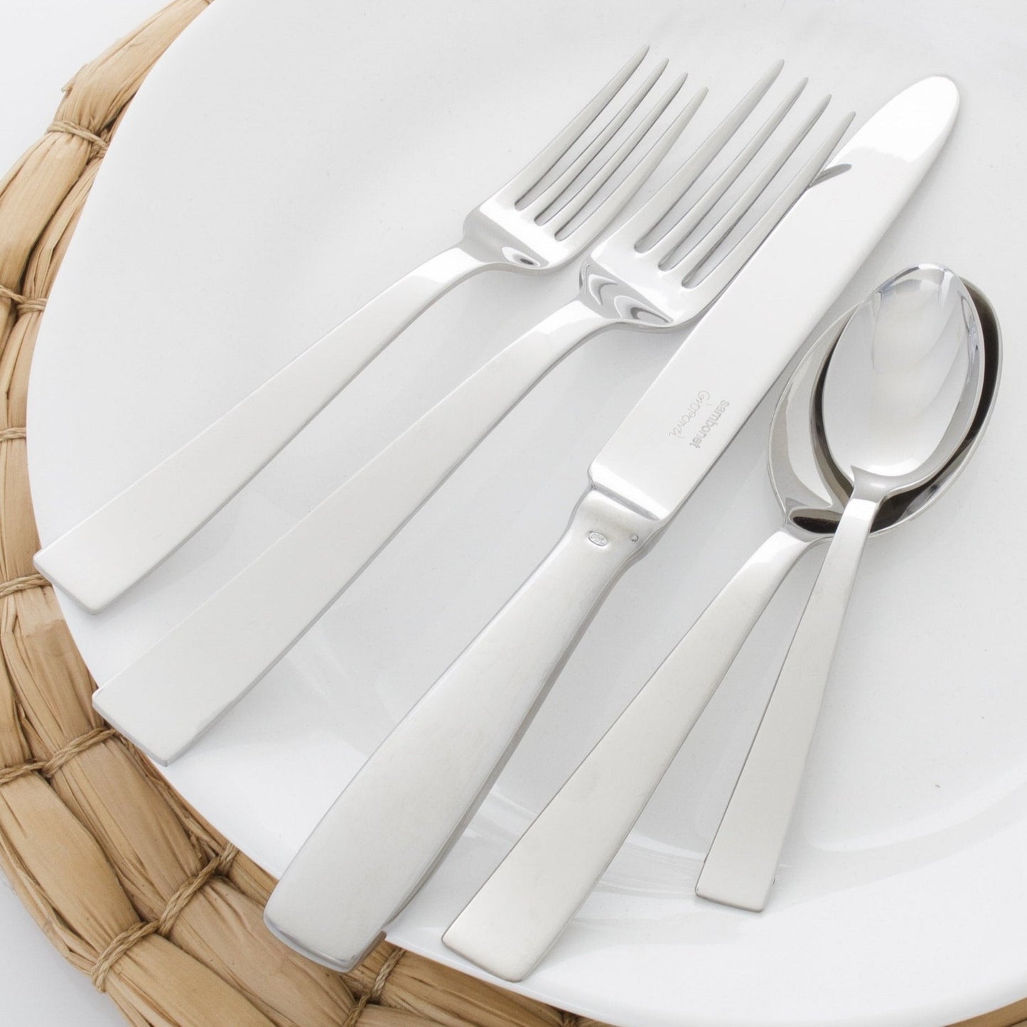 Gio Ponti 5-piece stainless steel flatware set with mirror finish on a white plate.