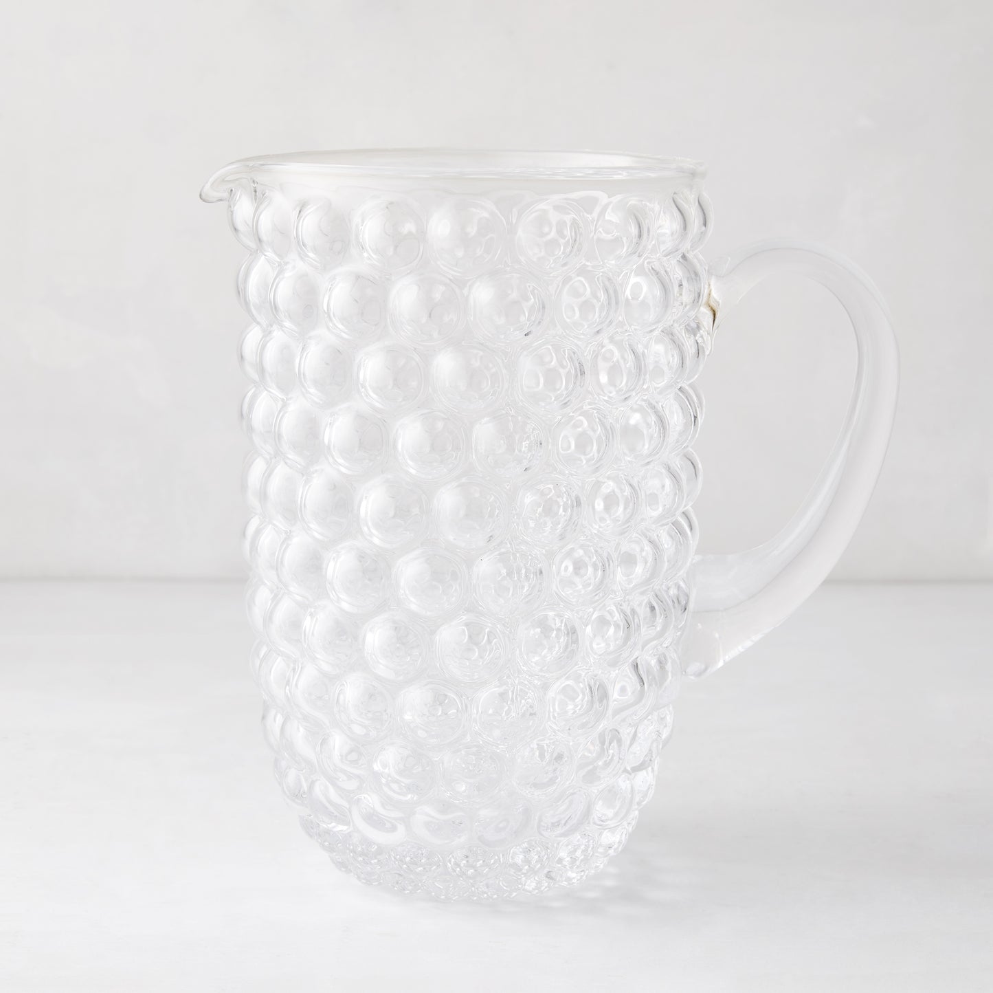 Clear glass pitcher with textured bubble design, handle, and pouring spout.