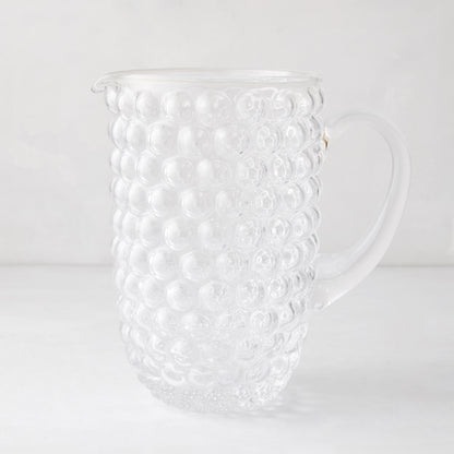 Clear glass pitcher with textured bubble design, handle, and pouring spout.