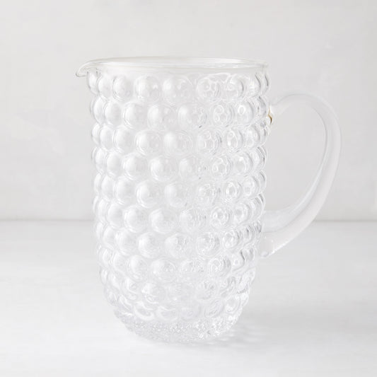 Clear glass pitcher with textured bubble design, handle, and pouring spout.