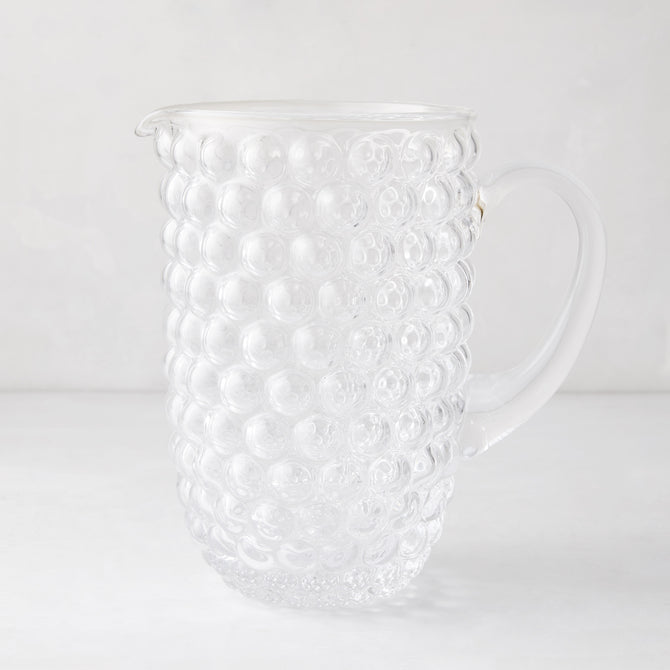 Clear glass pitcher with textured bubble design, handle, and pouring spout.