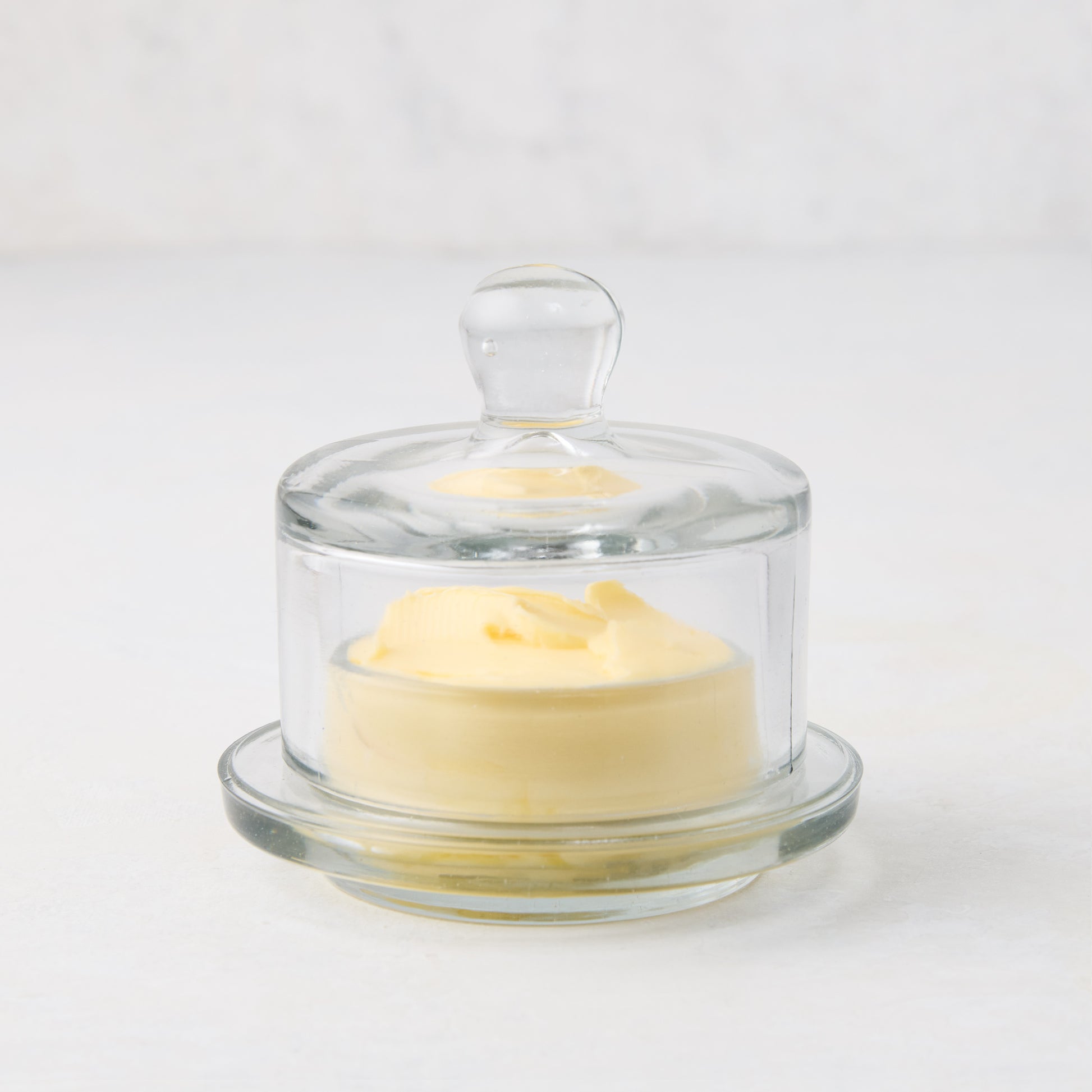 Clear glass butter dish with lid, 3.5"Dia x 3.5"H, holding a mound of yellow butter.