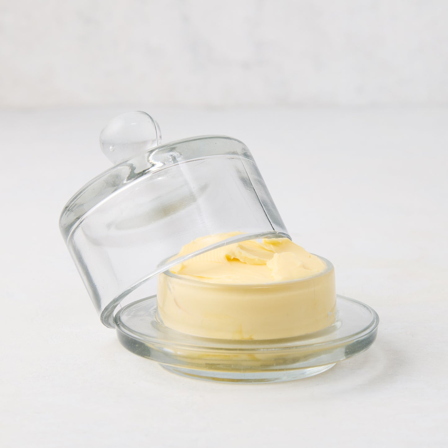 Clear glass butter dish with a domed lid and knob, holding yellow butter.
