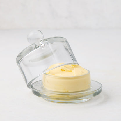 Clear glass butter dish with a domed lid and knob, holding yellow butter.