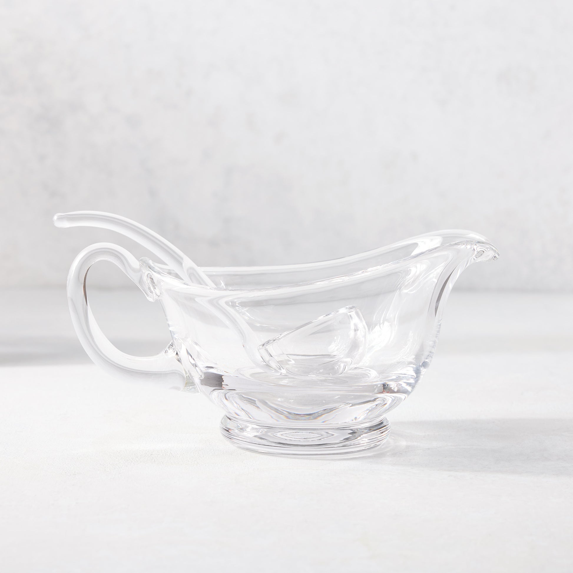 Clear glass gravy boat with handle, spout, and small glass ladle.