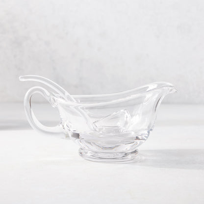 Clear glass gravy boat with handle, spout, and small glass ladle.