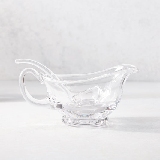 Clear glass gravy boat with handle, spout, and small glass ladle.