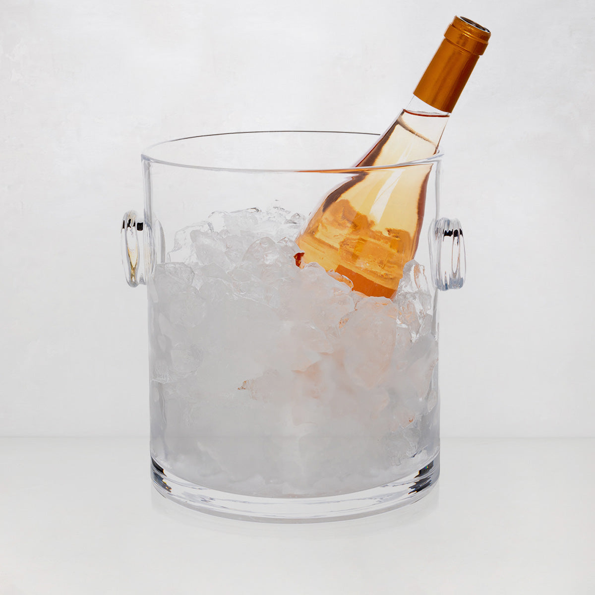 Handblown clear glass ice bucket with knob handles, filled with ice and a rose wine bottle.