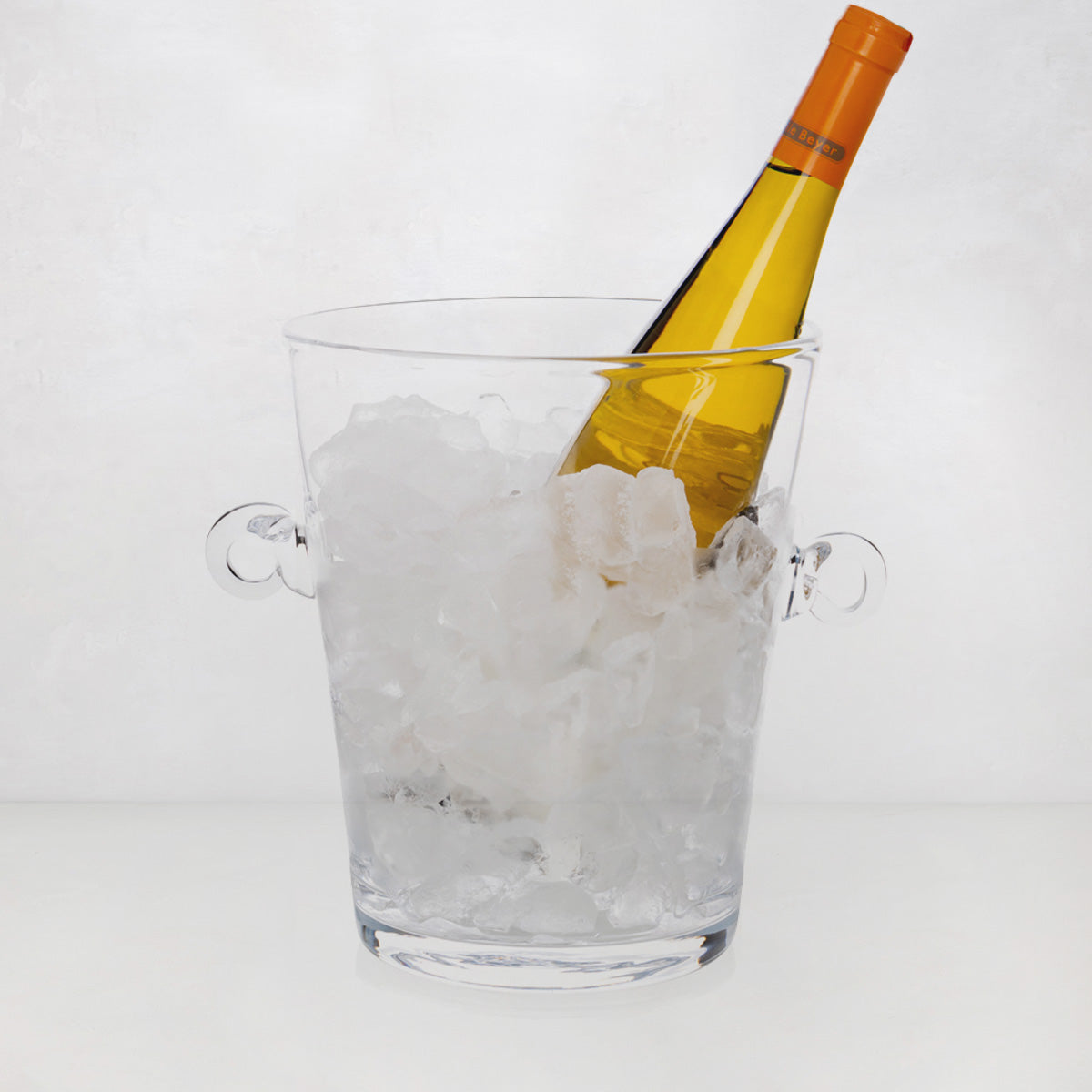 Handblown clear glass ice bucket with ring handles, filled with ice and a yellow wine bottle.
