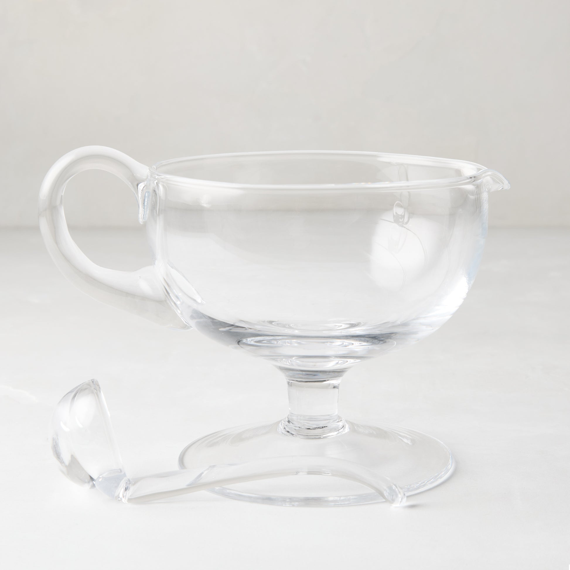 Clear glass sauce/gravy boat with handle, spout, pedestal base, and matching glass ladle.