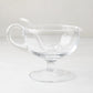 Clear glass sauce/gravy boat with handle, spout, pedestal base, and matching glass ladle.