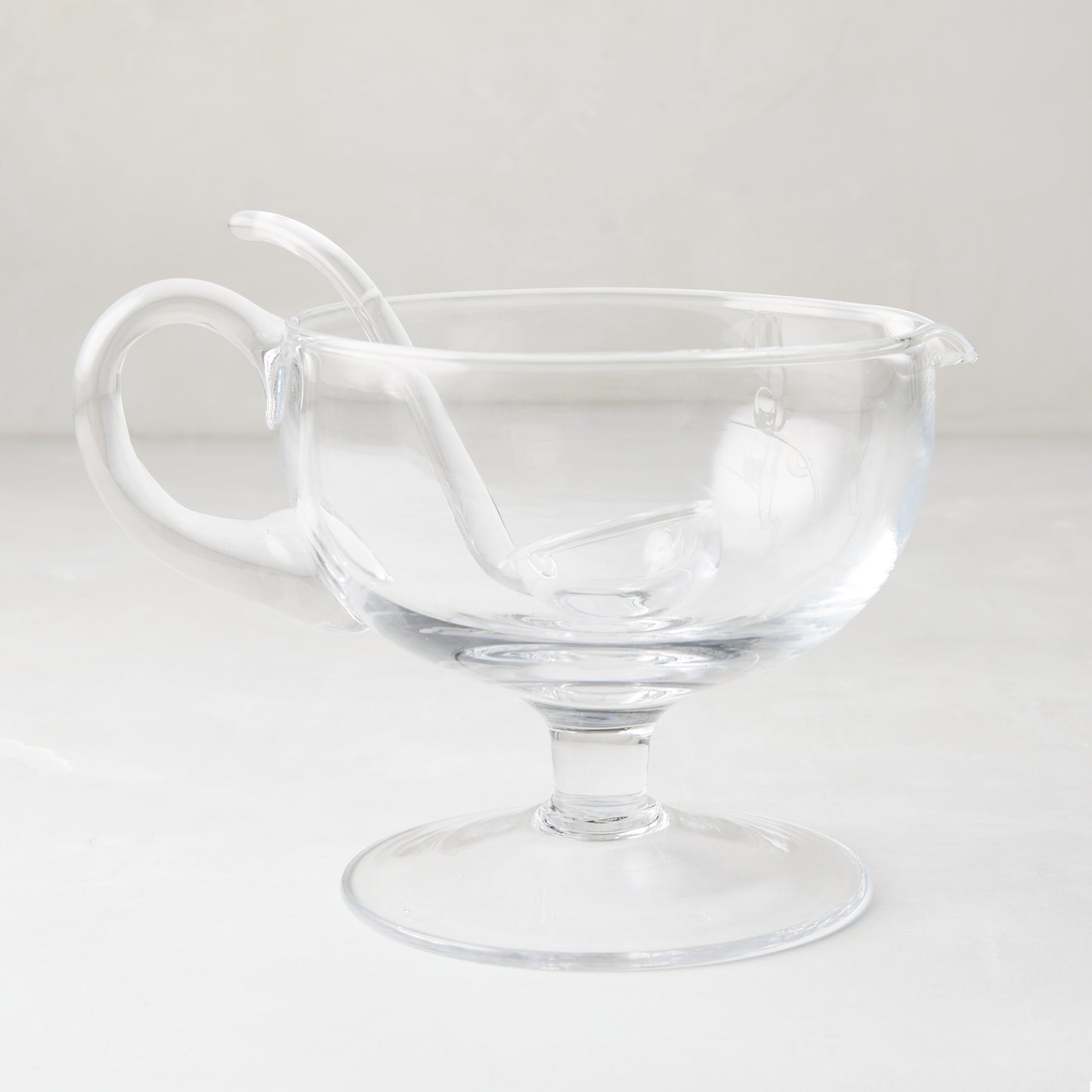 Clear glass sauce/gravy boat with handle, spout, pedestal base, and matching glass ladle.