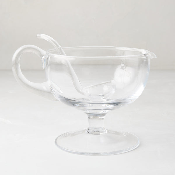 Clear glass sauce/gravy boat with handle, spout, pedestal base, and matching glass ladle.