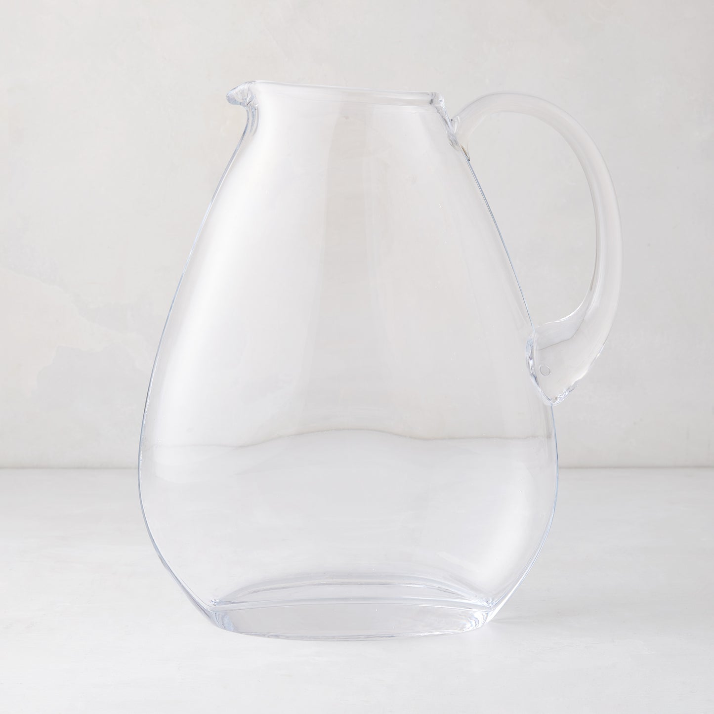 Clear, mouth-blown glass teardrop pitcher with handle and sturdy base.