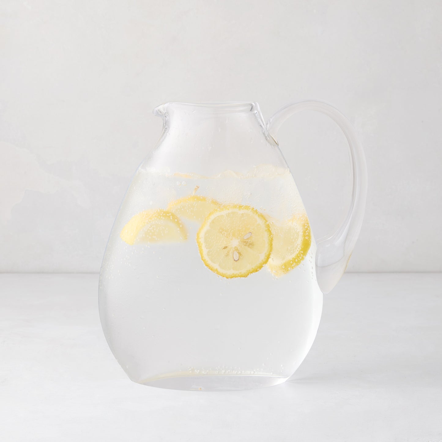 Clear glass teardrop pitcher filled with water and lemon slices, mouth-blown in Poland.