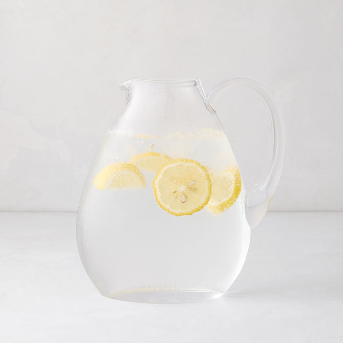 Clear glass teardrop pitcher filled with water and lemon slices, mouth-blown in Poland.