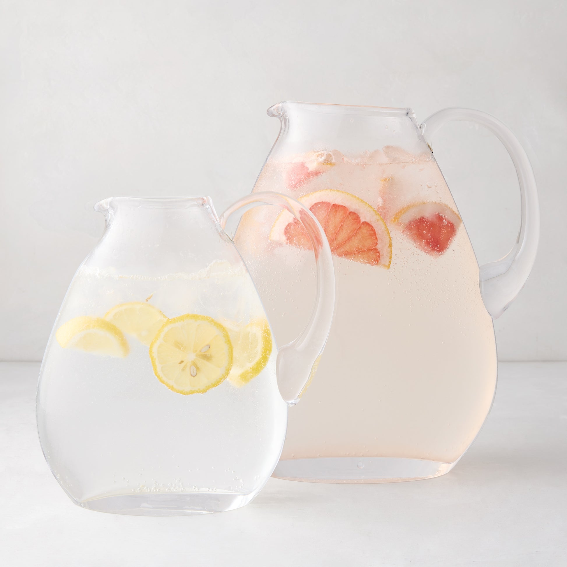 Two clear glass teardrop pitchers, one large with pink grapefruit drink, one small with lemon water.