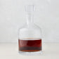 Clear mouth-blown glass wine and whiskey decanter with broad base, curved neck, and stopper, filled with amber liquid.