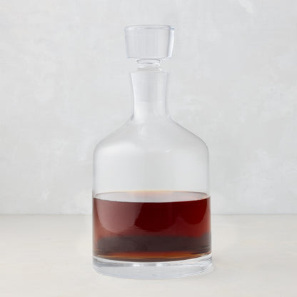Clear mouth-blown glass wine and whiskey decanter with broad base, curved neck, and stopper, filled with amber liquid.