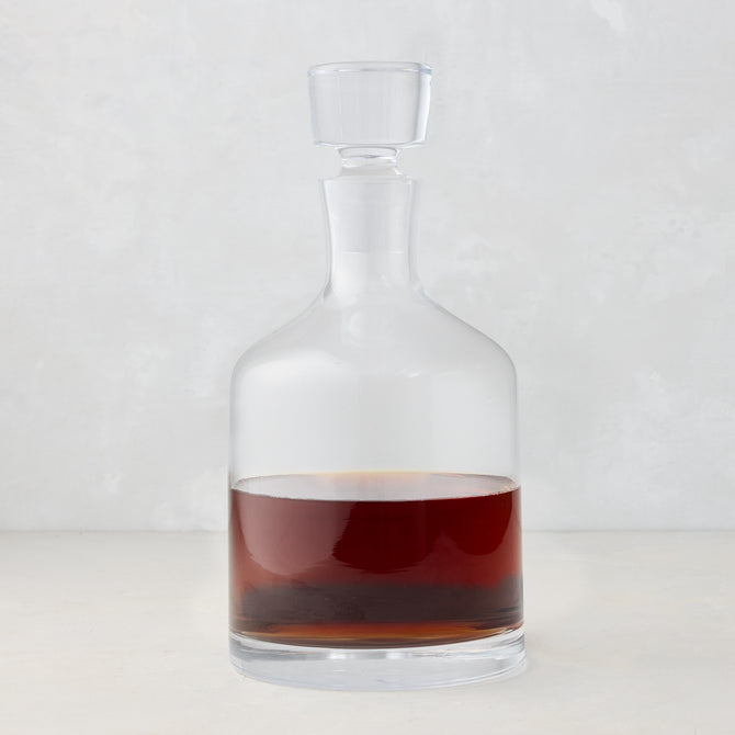 Clear mouth-blown glass wine and whiskey decanter with broad base, curved neck, and stopper, filled with amber liquid.