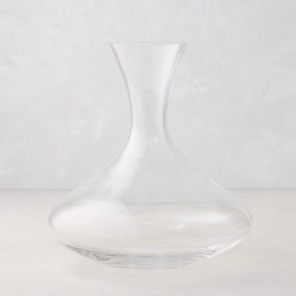 Clear mouth-blown glass wine carafe, 50 oz, with a broad base and curved neck.