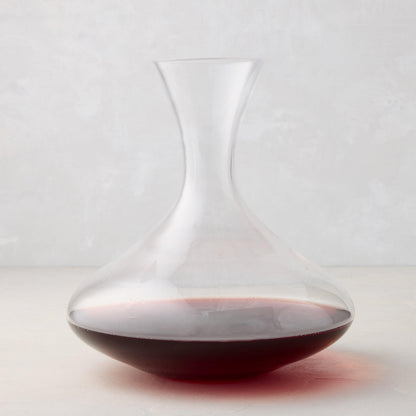 Clear mouthblown glass wine carafe with a broad base, curved neck, and red wine inside.