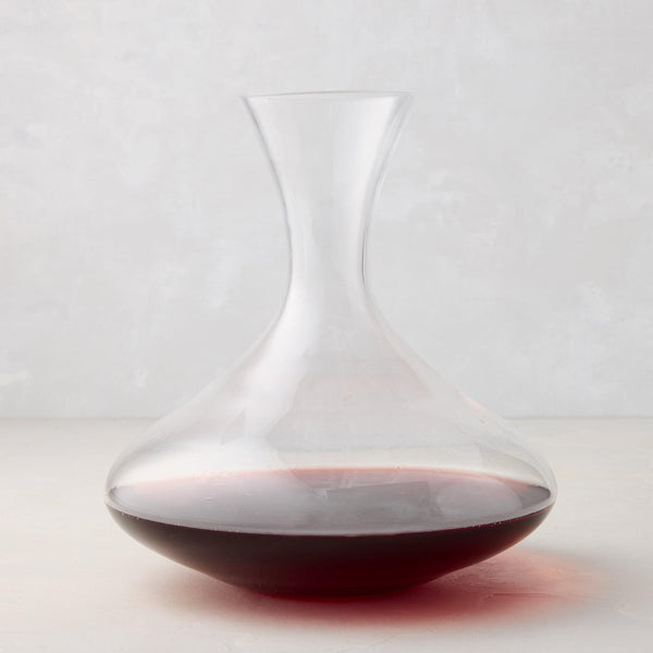 Clear mouthblown glass wine carafe with a broad base, curved neck, and red wine inside.
