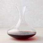 Clear mouthblown glass wine carafe with a broad base, curved neck, and red wine inside.