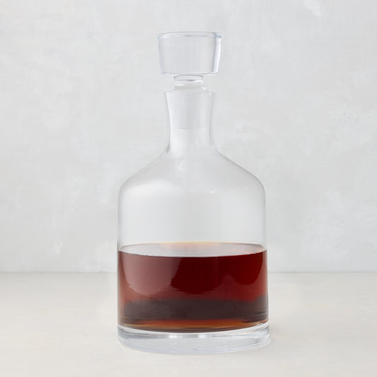 Clear mouth-blown glass wine and whiskey decanter with broad base, curved neck, and stopper, filled with amber liquid.