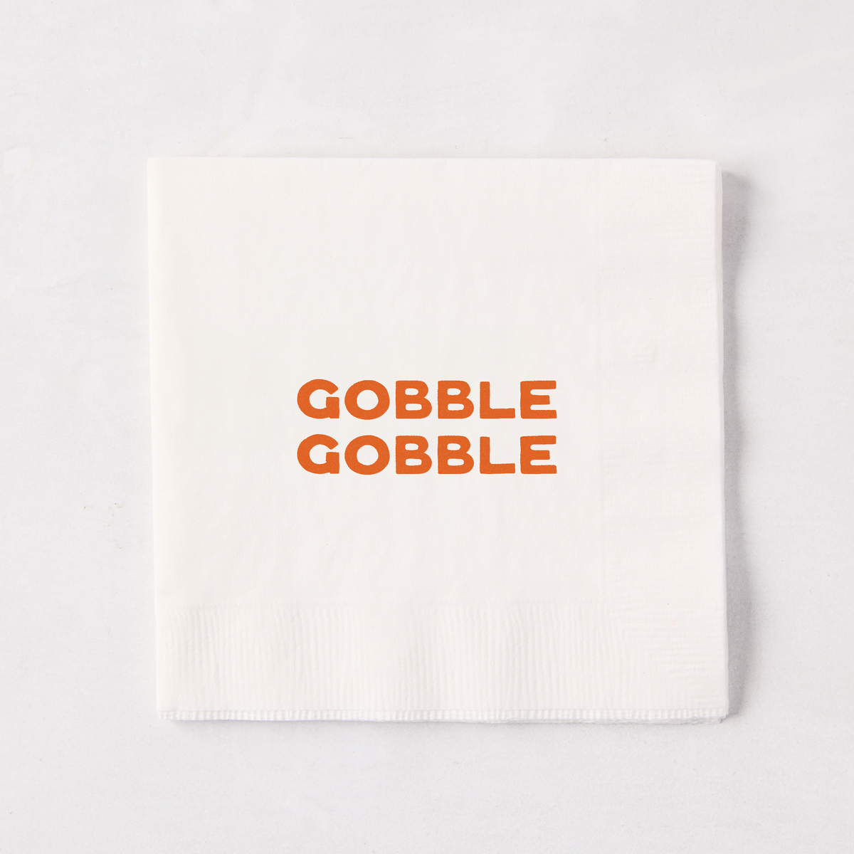 Square white paper cocktail napkin with orange Gobble Gobble text, 5.5 inches.