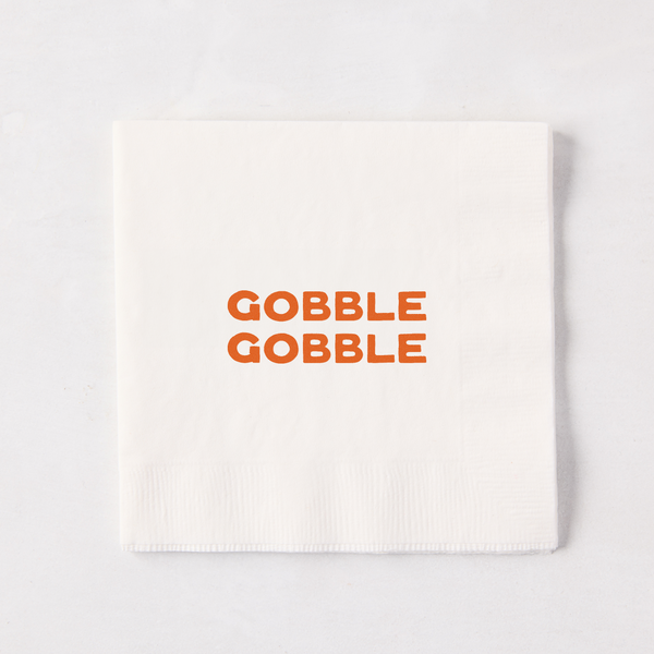 Square white paper cocktail napkin with orange Gobble Gobble text, 5.5 inches.