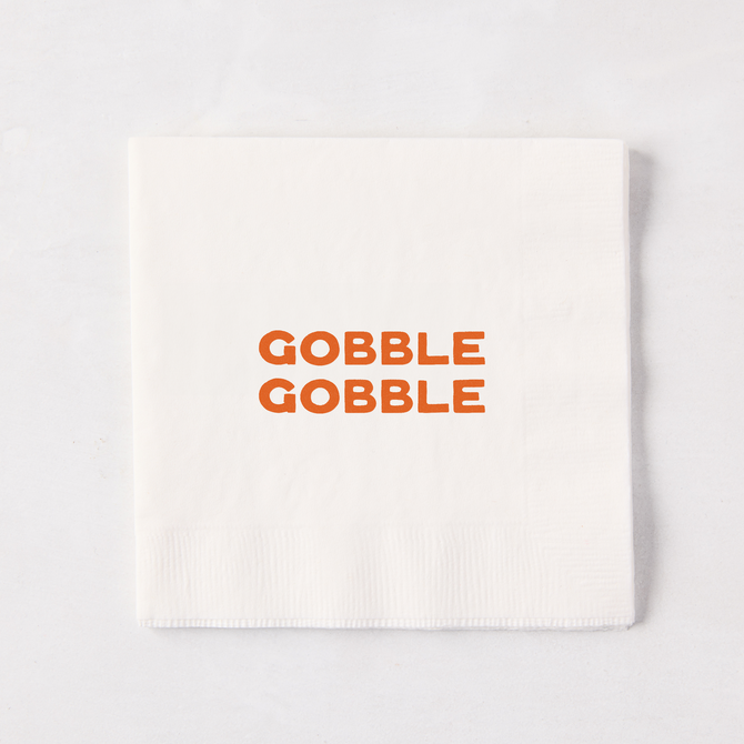 Square white paper cocktail napkin with orange Gobble Gobble text, 5.5 inches.