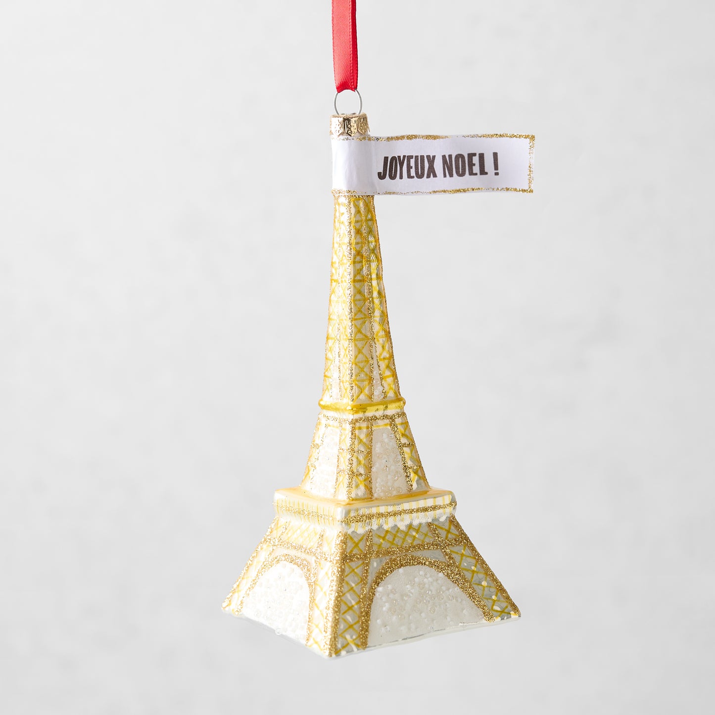 Gold glittered glass Eiffel Tower Christmas ornament with a Joyeux Noel sign, 5.75 inches tall.