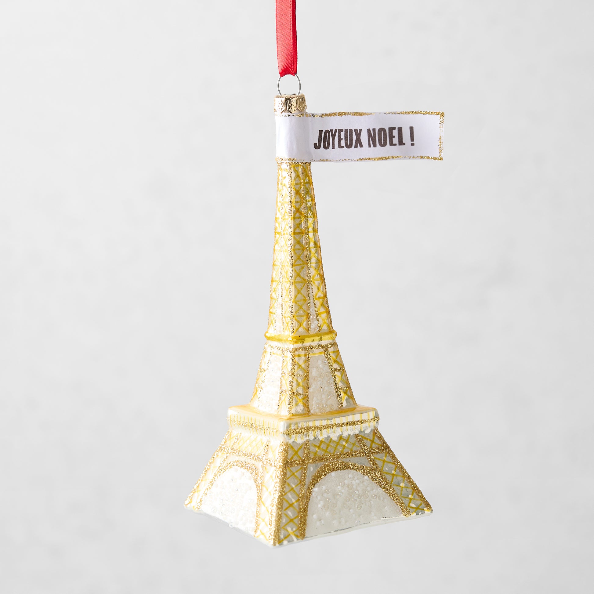 Gold glittered glass Eiffel Tower Christmas ornament with a Joyeux Noel sign, 5.75 inches tall.