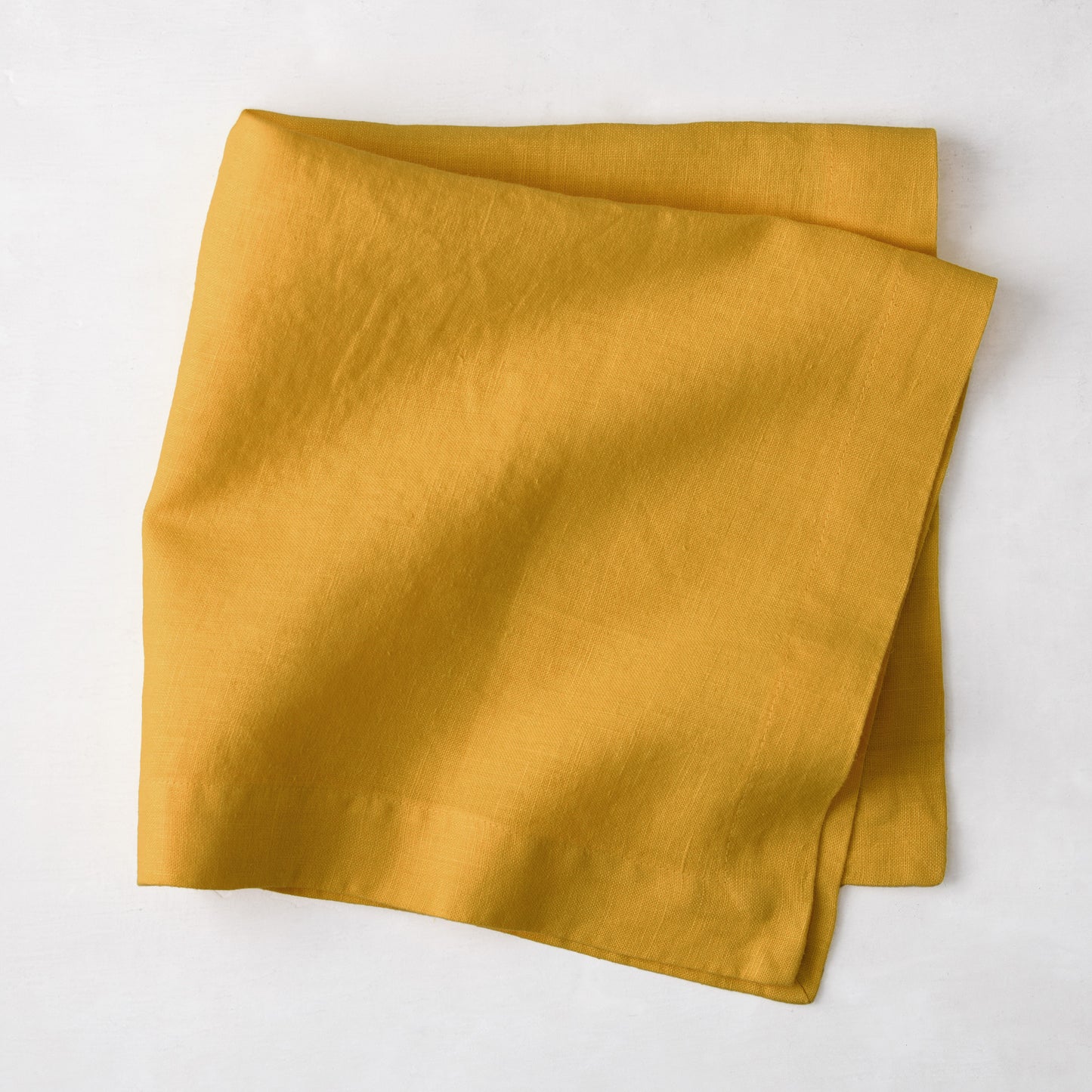 Golden Mustard HG Signature Hand-dyed Linen Napkin, 22-inch square, folded on a white surface.