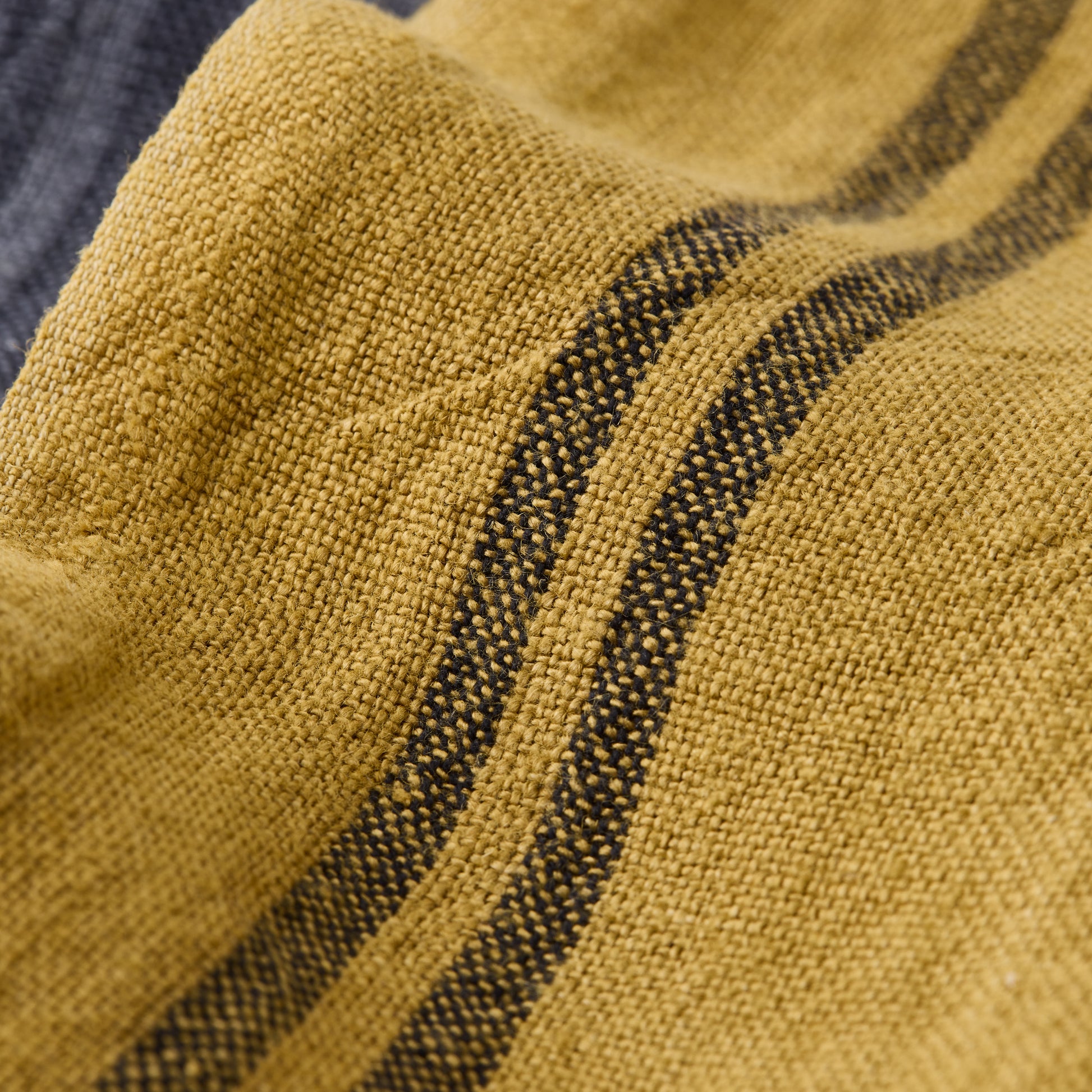 Goldenrod yellow French linen tea towel with dark striped pattern, close-up of fabric texture.