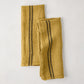 Set of 2 goldenrod yellow French linen tea towels with dark vertical stripes, one folded.