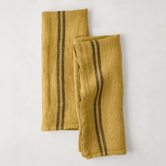 Set of 2 goldenrod yellow French linen tea towels with dark vertical stripes, one folded.