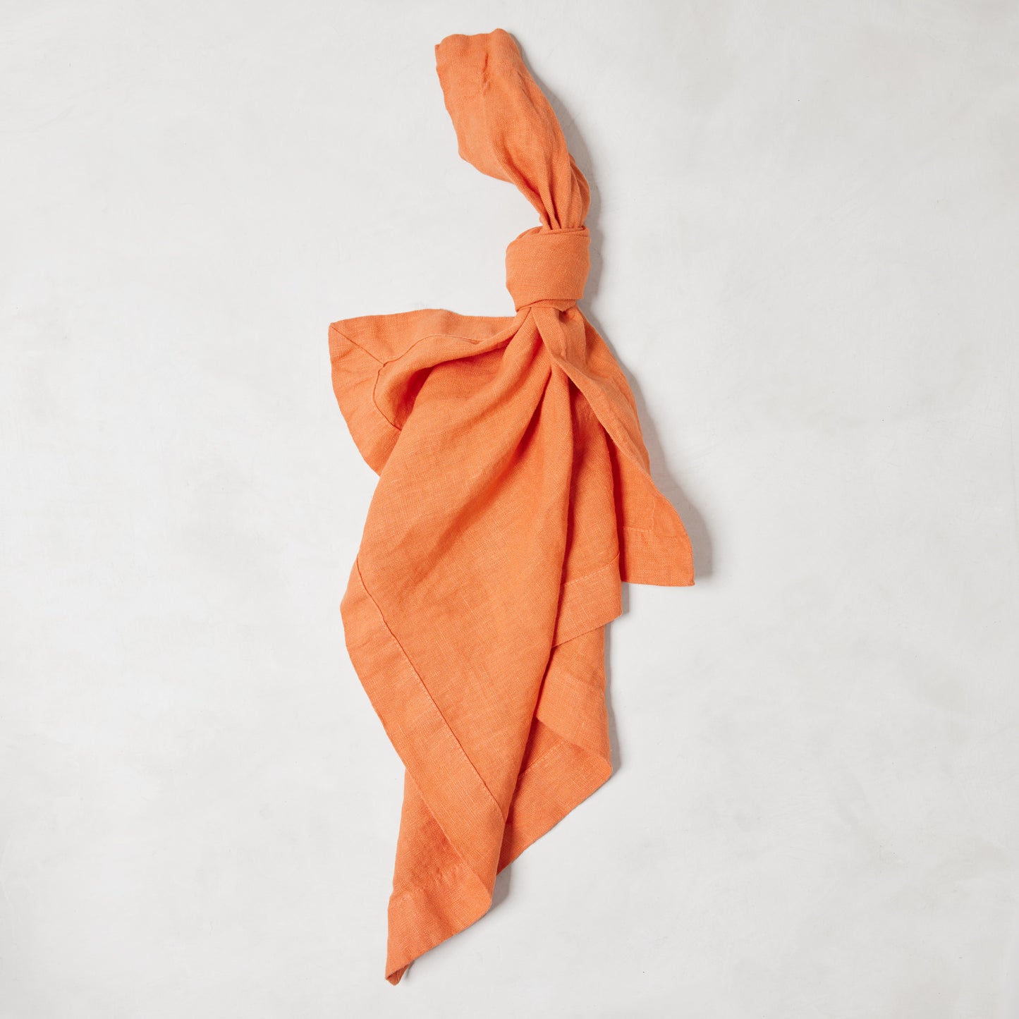 Goldfish HG Signature hand-dyed linen napkin, 22-inch square, tied in a knot on a white surface.