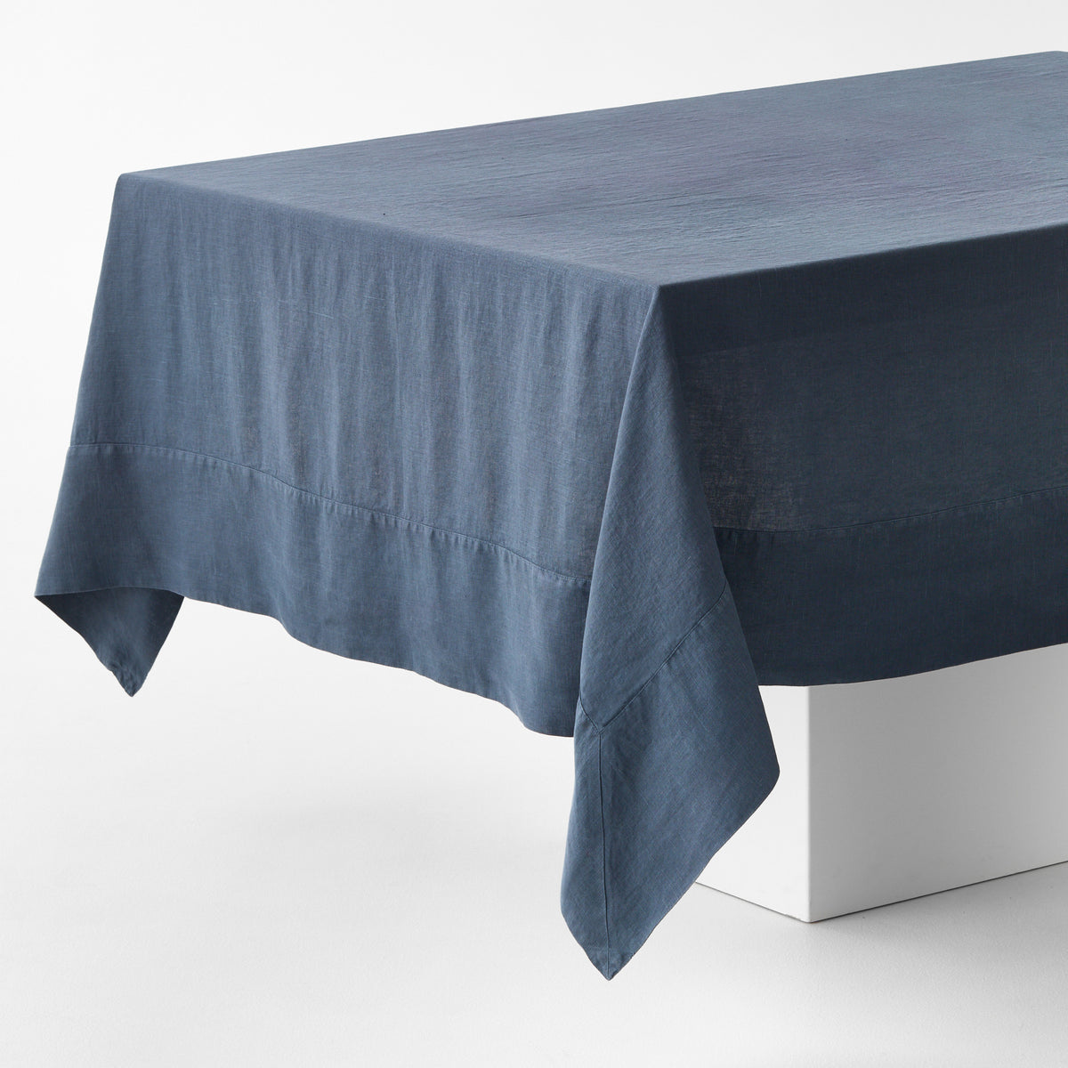 Graphite hand-dyed linen tablecloth with a wide border and mitered corner detailing on a white display block.