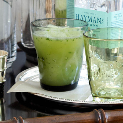 Grey Henri mouth-blown glass with green drink, next to an empty green Henri glass on a silver tray.