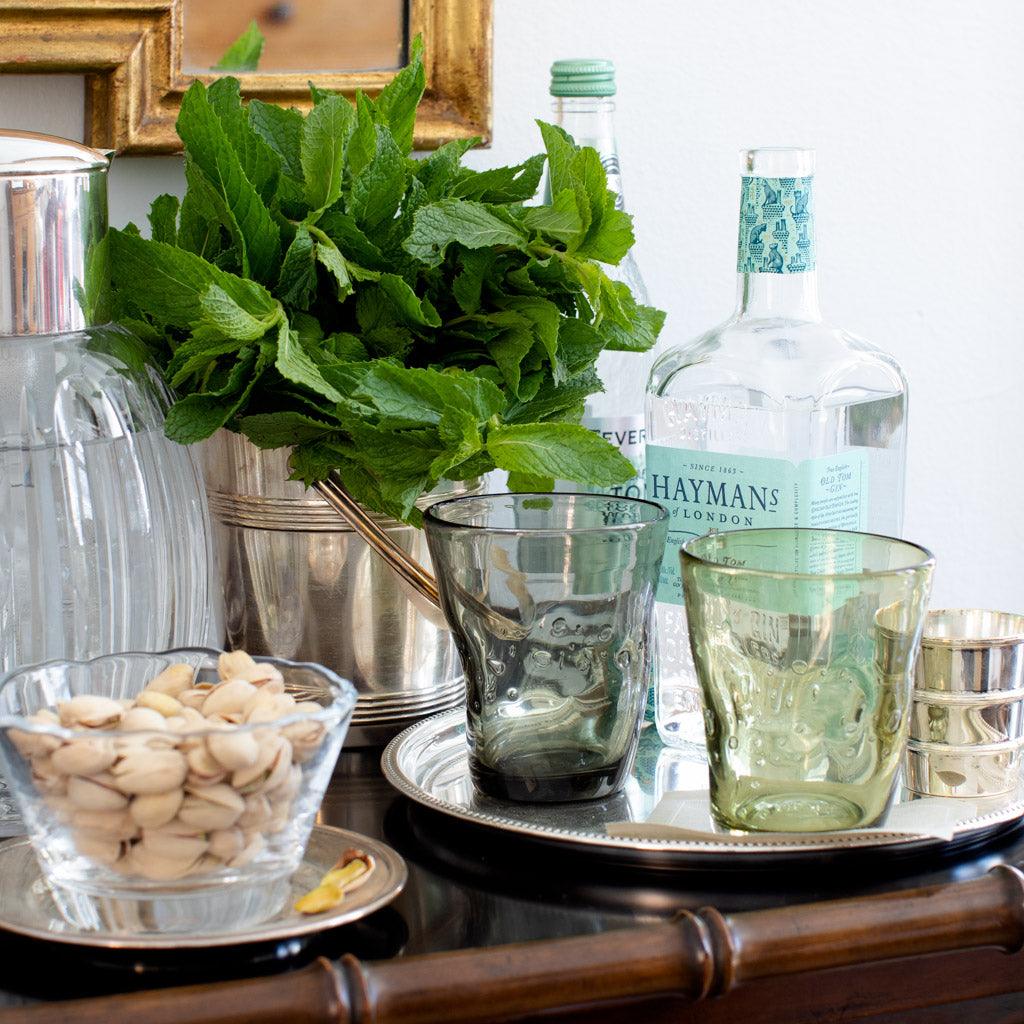 Grey Henri 8 oz. mouth-blown glass with textured surface, next to a green glass, pistachios, and mint.